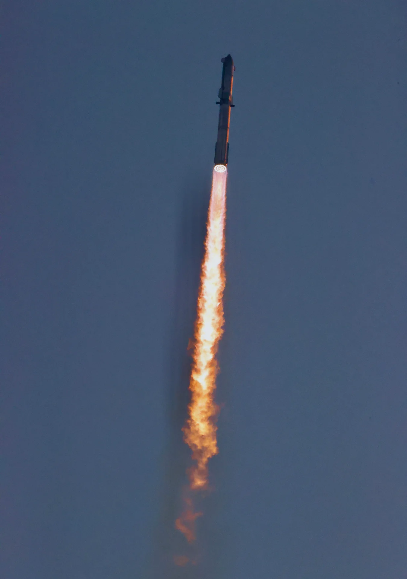 Starship ascends through a deep blue sky above a long orange exhaust plume.